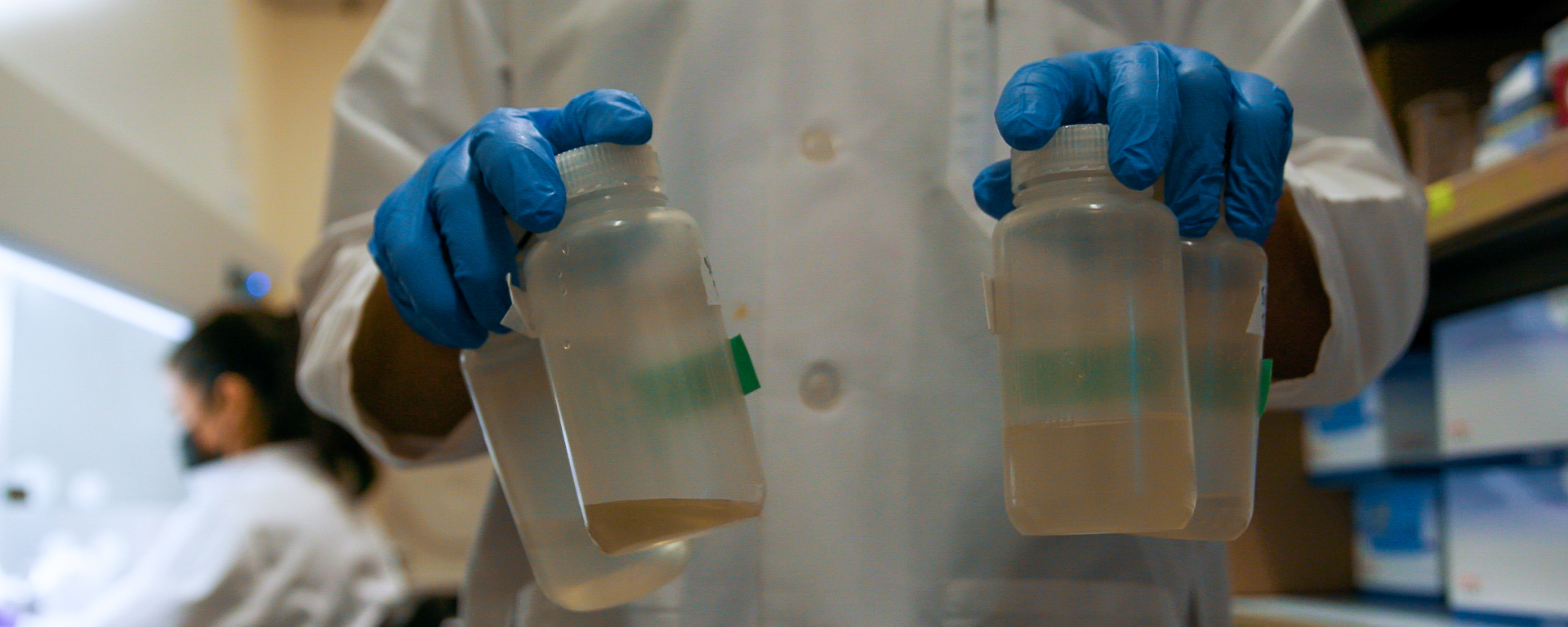 Two hands holding four test tubes with wastewater in a science lab.