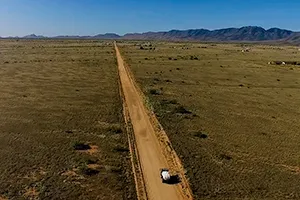 drone shoot of car on dirt road with mountains behind