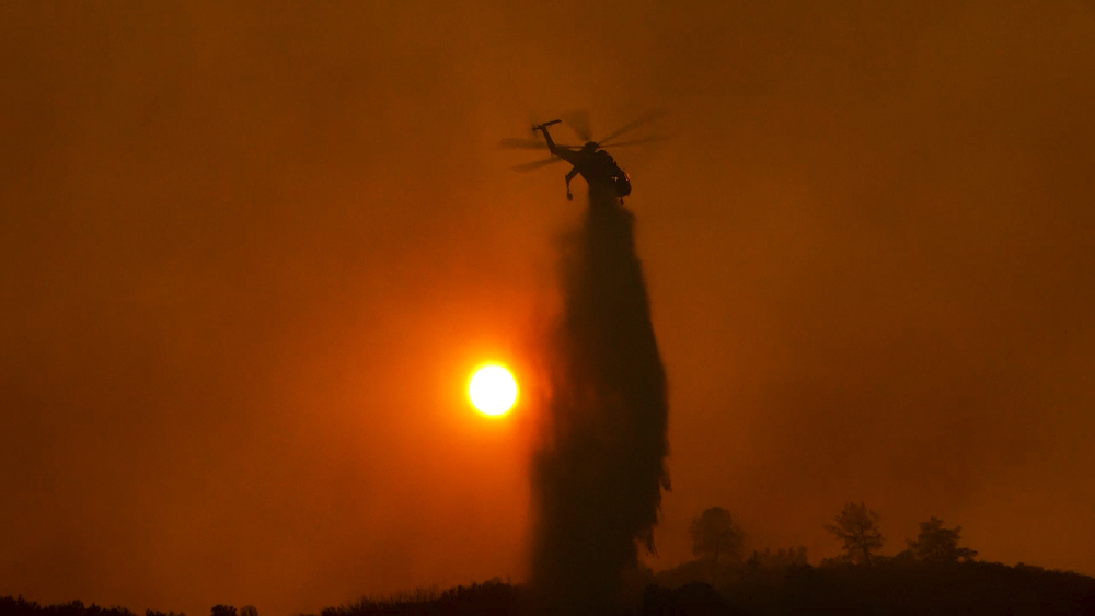 Helicopter dumping water on wildfire in sunset